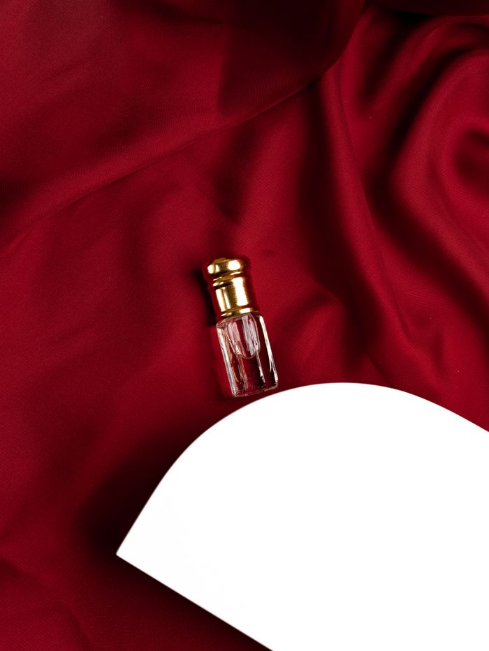 our-story A glass perfume bottle rests elegantly on luxurious red silk fabric, accompanied by a white platform.