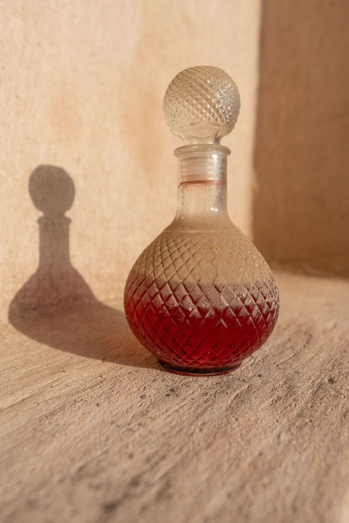 who-we-are A beautifully crafted crystal decanter filled partly with red liquid casting a shadow in warm sunlight.
