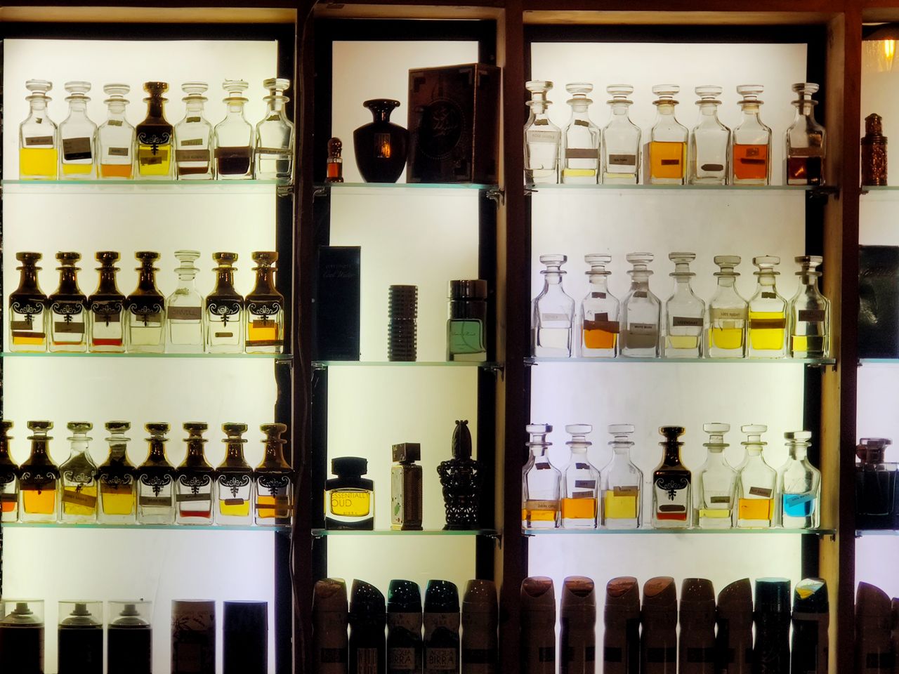 services-03 Aesthetic arrangement of diverse perfume bottles on illuminated shelves showcasing luxury fragrances.