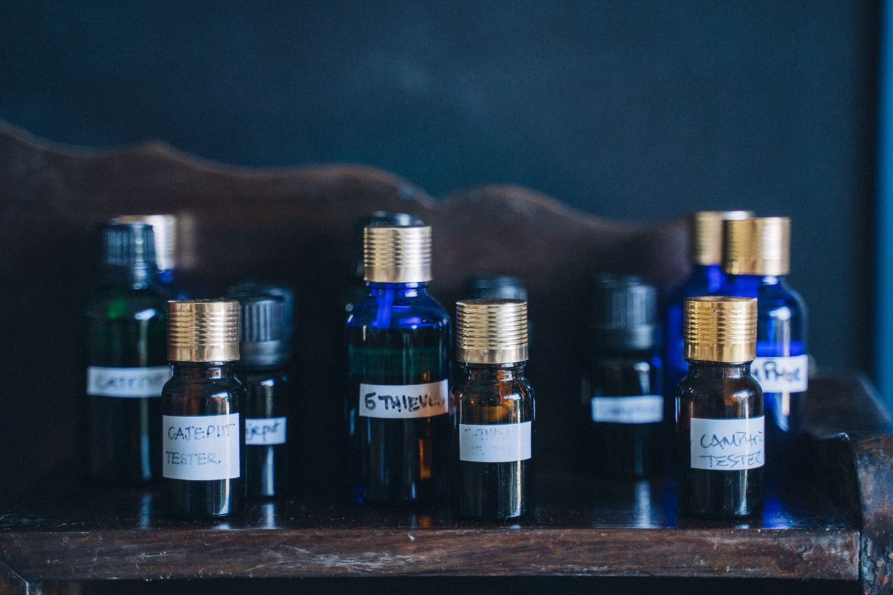 services-04 Close-up of glass bottles with essential oils arranged on a wooden shelf, labeled with various oils.